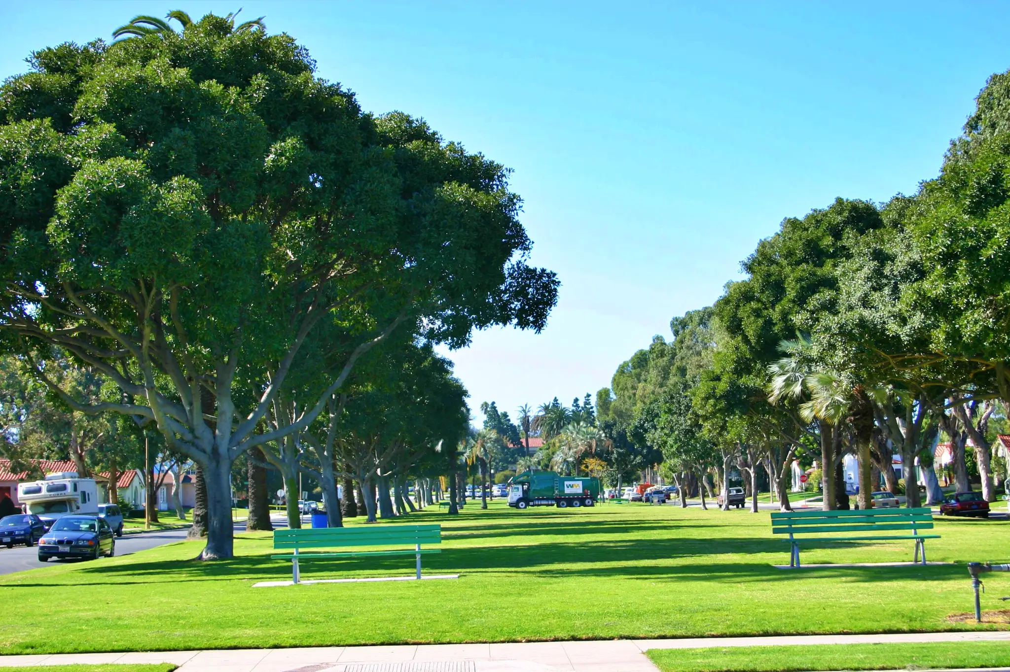 Neighborhood park in El Segundo, California with a blue-shaded playground, red and orange slides, picnic table, green grass, and surrounding residential homes